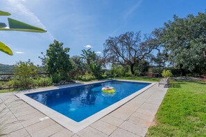 Una piscina rectangular con una superficie de agua azul cristalina, rodeada por una terraza empavedada.