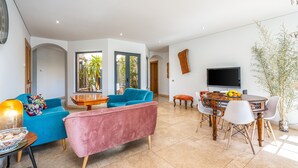 Ein modernes Wohnzimmer mit Sofa, Sessel, Esstisch und Fernseher.