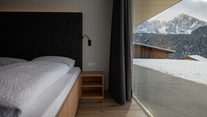 A bedroom with a bed, a bedside table, a window with a view of mountains.