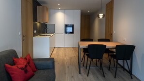 A modern kitchen with a dining area, a sofa with red cushions, and a ceiling light fixture.