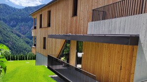 A modern wooden house with a balcony, surrounded by a well-maintained lawn and a mountainous backdrop.