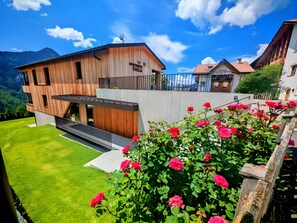A modern two-story building with a wooden facade, a balcony, and a well-maintained lawn.