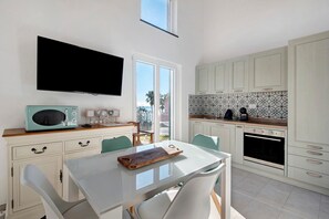 Une cuisine moderne avec des meubles blancs, un téléviseur à écran plat, un four à micro-ondes et un coin repas comprenant une table et des chaises.