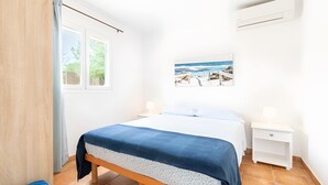 Een slaapkamer met een bed, een nachtkastje, een raam en een aan de muur bevestigde airconditioning.