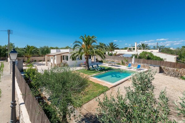 A residential property with a swimming pool, palm trees, and a fenced yard.