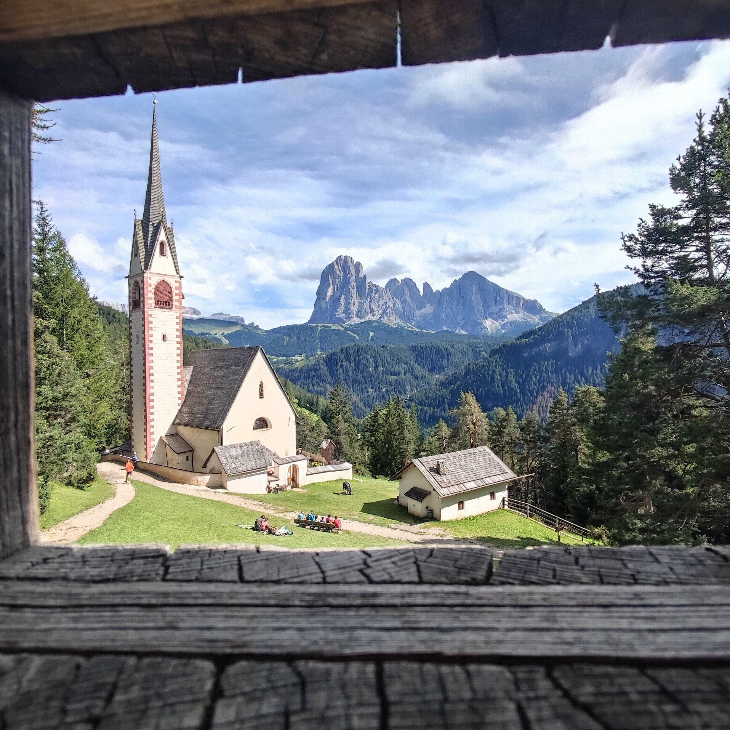 A church with a tall spire, surrounded by a small village with a mountain backdrop.