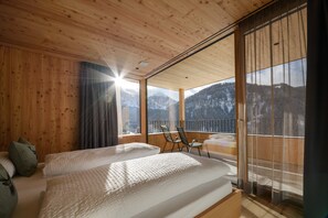 Et værelse med trævægge og -loft, en seng med hvid sengetøj, en stol og en balkon med udsigt til bjerge.