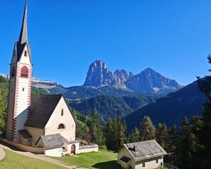 A church with a bell tower, a small chapel, and a mountain backdrop. - Apartment 'Apartments Emilia 2' with Mountain View, Balcony and Wi-Fi (Ortisei)
