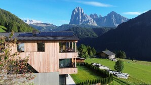 Ein modernes Holzgebäude mit Balkon, Solaranlage und Blick auf Berge.