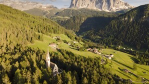 Eine gebirgige Landschaft mit Kirche, Häusern und einem markanten Felsgipfel.