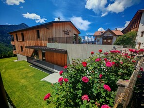 A modern wooden building with a balcony, surrounded by lush greenery and a clear blue sky. - Apartment 'Apartments Emilia 2' with Mountain View, Balcony and Wi-Fi (Ortisei)