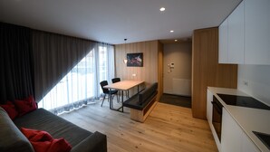 A modern living room with a sofa, a dining table, and a bench. There is a kitchen area with a stove and cabinets. - Apartment 'Apartments Emilia 3' with Mountain View, Balcony and Wi-Fi (Ortisei)
