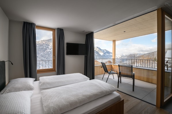 Une chambre avec deux lits, une télévision et un balcon offrant une vue sur la montagne.
