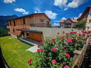 Un bâtiment moderne en bois, doté d’un balcon, entouré d’une végétation luxuriante et surplombé d’un ciel bleu azur.