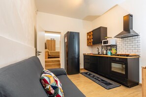 Ein kompakter Wohnraum mit einer Küchenzeile, einem Sofa mit bunter Decke und einer Treppe zu einem weiteren Raum.