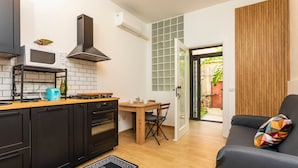 Une cuisine compacte équipée d’un four à micro-ondes, d’une cuisinière et d’un four, une table à manger avec des chaises, et un canapé agrémenté d’un coussin coloré.