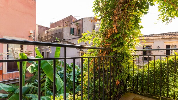 A balcony with a metal railing, lush green plants, and a view of neighboring buildings. - Apartment 'La Dimora Di Via Manzoni' with Private Terrace, Wi-Fi and Air Conditioning (Catania)