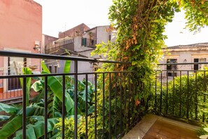 Un balcon doté d’une rambarde en métal, agrémenté de plantes luxuriantes et offrant une vue sur les bâtiments voisins.