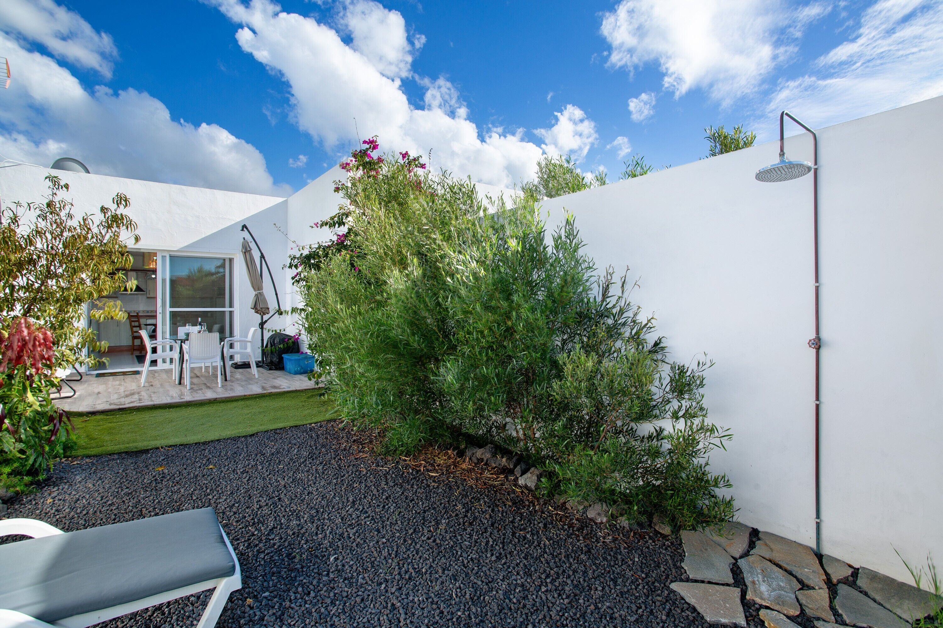 Un patio moderno al aire libre con una zona de estar, un pequeño jardín y una pared blanca.