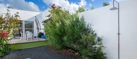 Un patio moderno al aire libre con una zona de estar, un pequeño jardín y una pared blanca.