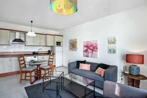 A modern kitchen with a dining area, a living room with a sofa and a coffee table, and a small side table with a lamp.