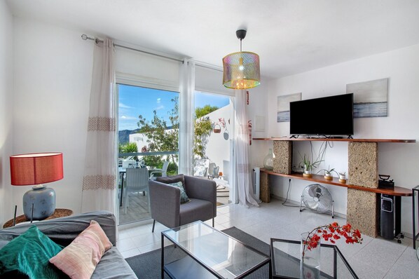 A modern living room with a sofa, armchair, glass coffee table, and a TV on a wooden shelf.