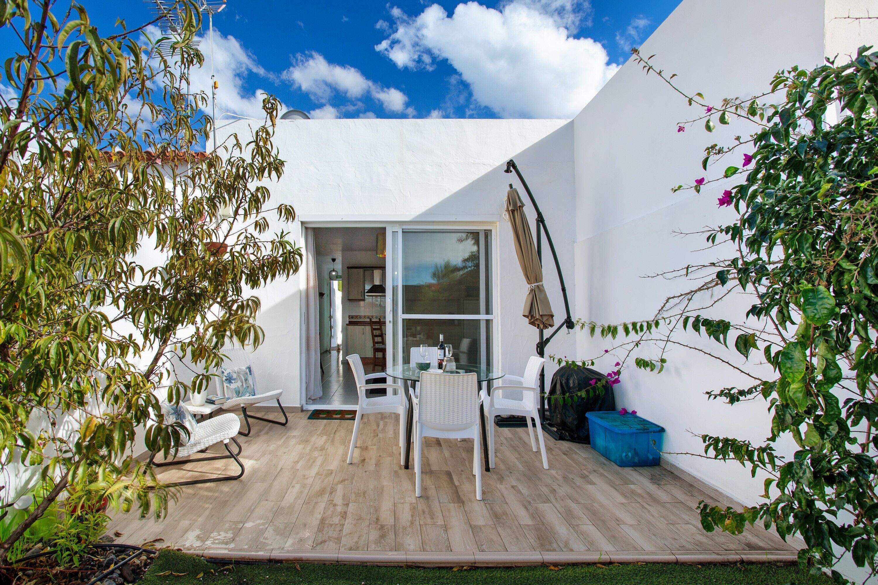 A patio with a table and chairs, a white wall, and a door leading to an interior space.