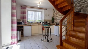 Una cocina con una escalera de madera, una pared de piedra y un ventanal con cortinas.