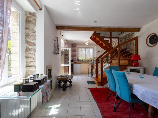 A spacious kitchen with a wooden staircase, a dining area with blue chairs, and a red rug.
