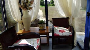 Una habitación con una mesa, dos sillas de mimbre, una planta en maceta y un florero con flores.
