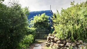 Un sendero en un jardín que lleva a un edificio azul con cerca de madera y pared de piedra.
