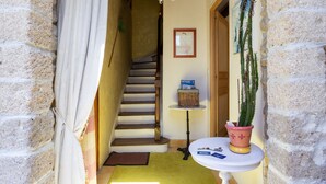 A narrow hallway with a staircase, a small table with a potted cactus, and a chandelier.