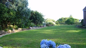 A well-maintained lawn with a stone border and a potted hydrangea plant in the foreground.