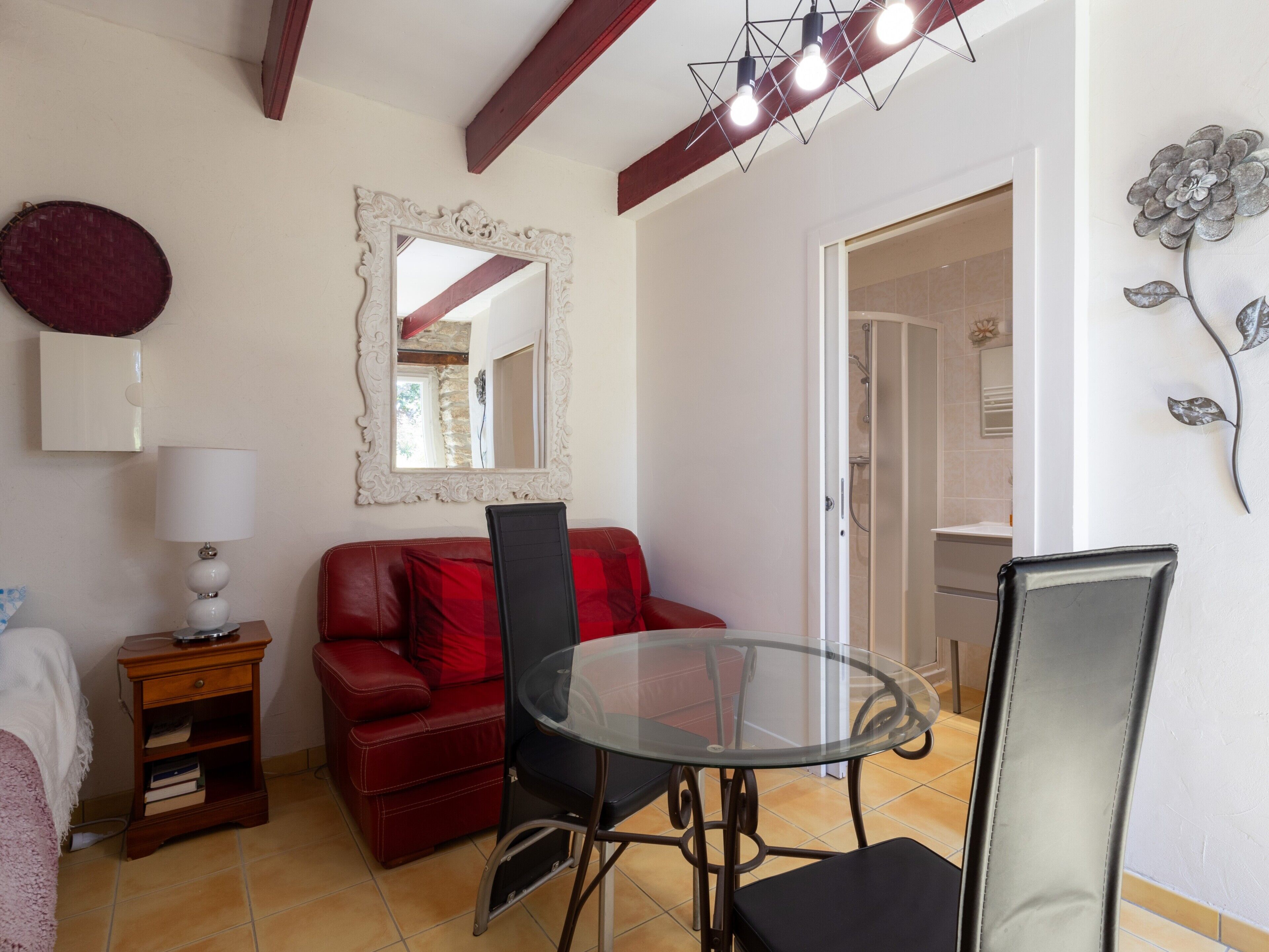 A room with a glass table, red leather sofa, a white cabinet, and a mirror on the wall.