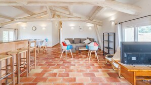 A spacious room with a tiled floor, wooden ceiling beams, a sofa set, and a television on a wooden table.