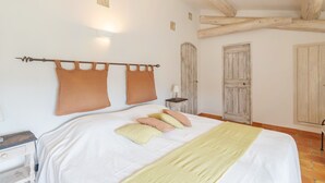 A bedroom with a bed, pillows, a nightstand, a lamp, and wooden beams on the ceiling.