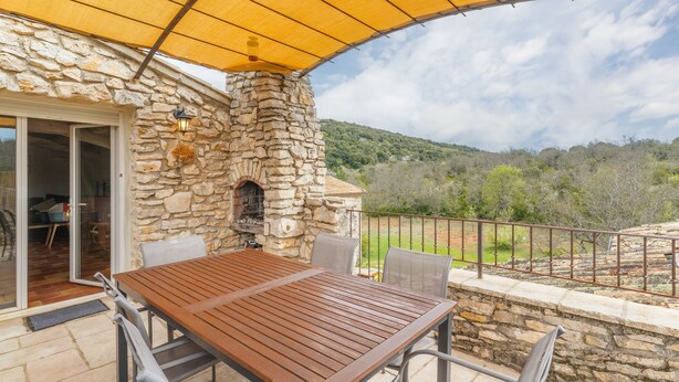 A stone building with a wooden table and chairs, a stone oven, and a view of the surrounding landscape.
