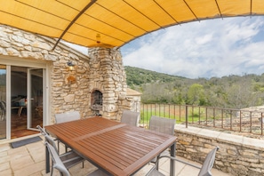 A stone building with a wooden table and chairs, a stone oven, and a view of the surrounding landscape.