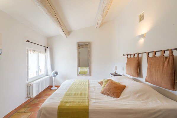 A bedroom with a bed, a bedside table, a mirror, a radiator, and a window with curtains.