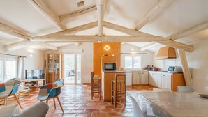 A spacious living area with a high ceiling, a kitchen with modern appliances, and a dining area with a table and chairs.
