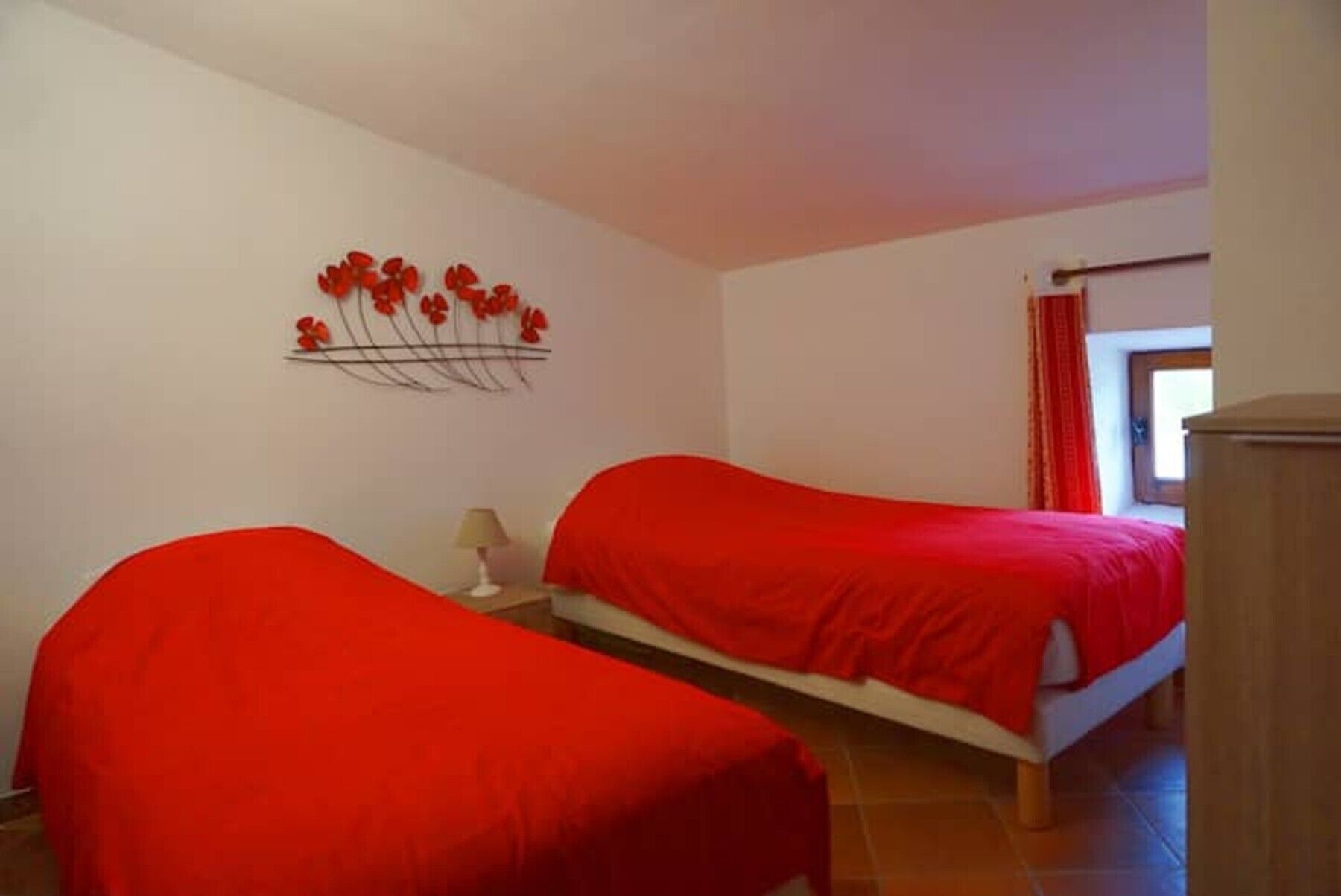 A bedroom with two beds, a wall art piece, a lamp, and a window with curtains.