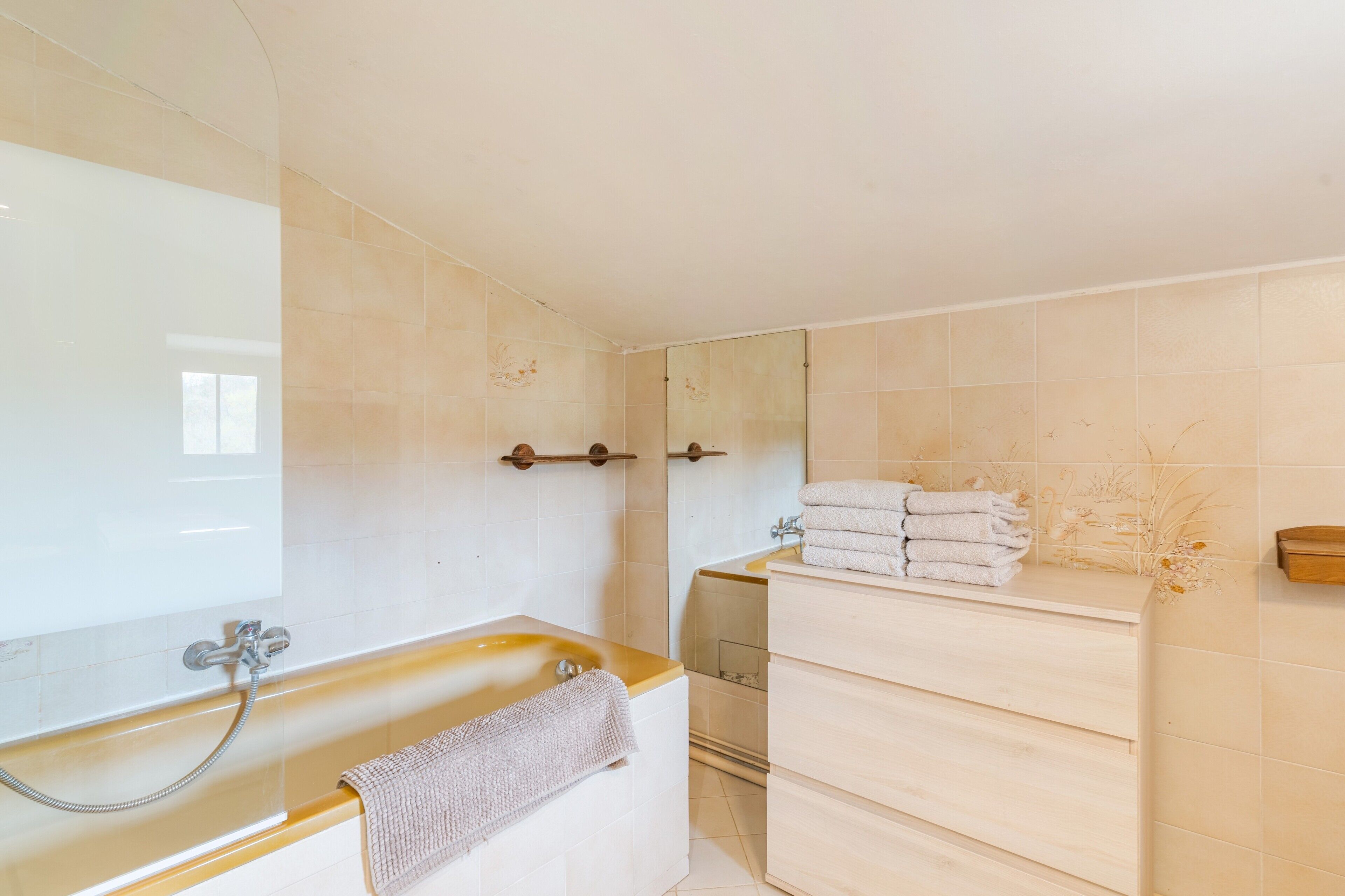 A bathroom with a bathtub, a mirror, a towel rack, and a wooden vanity.