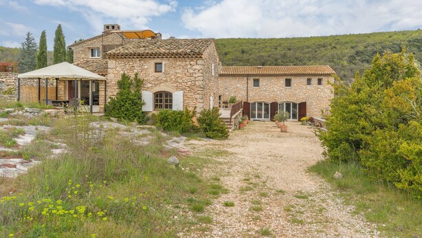 Un edificio de piedra con un camino de grava, un espacio de estar al aire libre cubierto y vistas a una colina.