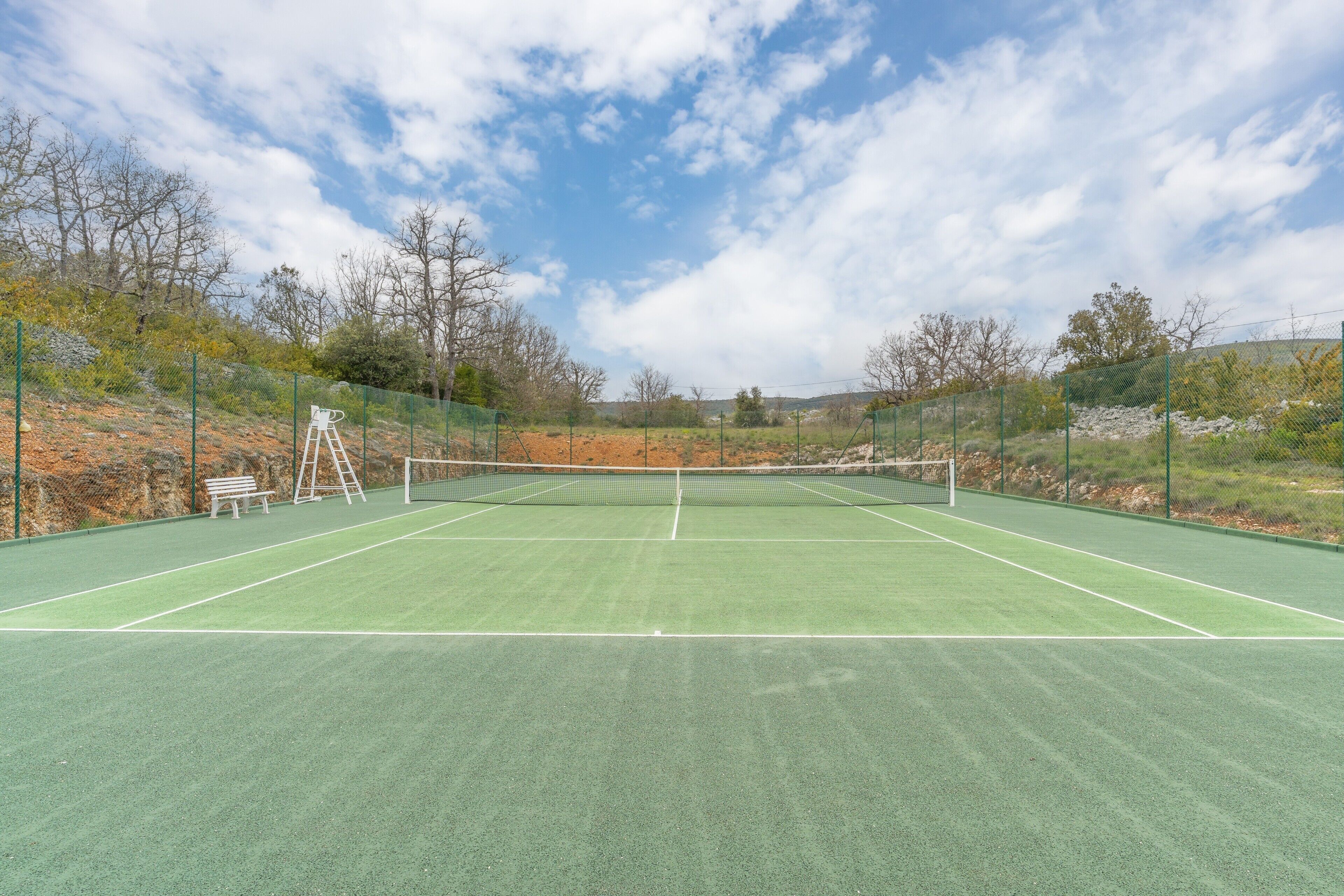 En tennisbane med net, bænke og en stige.