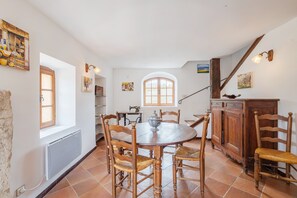 Un coin repas avec une table ronde, des chaises en bois, un radiateur, une fenêtre et un escalier.