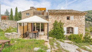 Una casa de piedra con un patio, mobiliario de exterior y una zona cubierta.