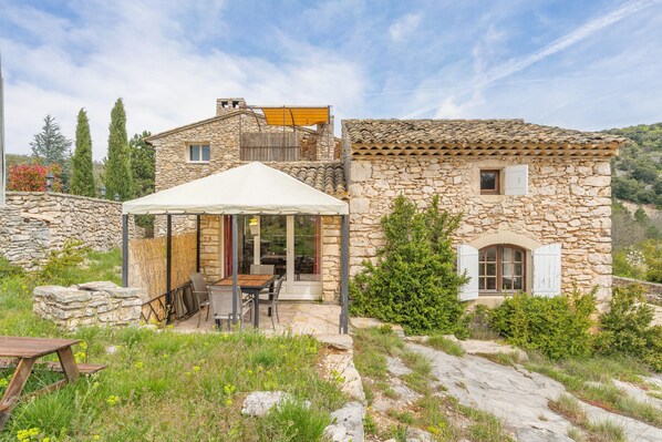 Une maison en pierre dotée d’un patio, d’un espace extérieur aménagé pour s’asseoir et d’une zone couverte.
