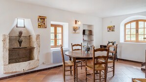 Un comedor con chimenea de piedra, sillas de madera, una mesa redonda y un ventanal con vistas.