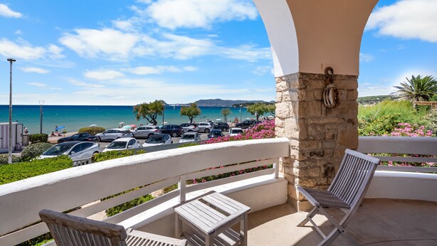 Un balcon avec vue sur la mer, des voitures garées et un pilier en pierre.