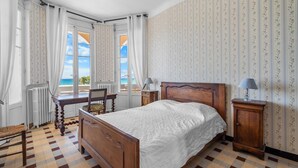 Une chambre à coucher avec un lit, un bureau, une chaise, un radiateur et une fenêtre avec des rideaux.